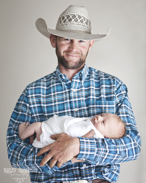 cowboy smiling and holding baby boy, rustic and natural posed newborn photography in Ellensburg WA by Hailey Haberman